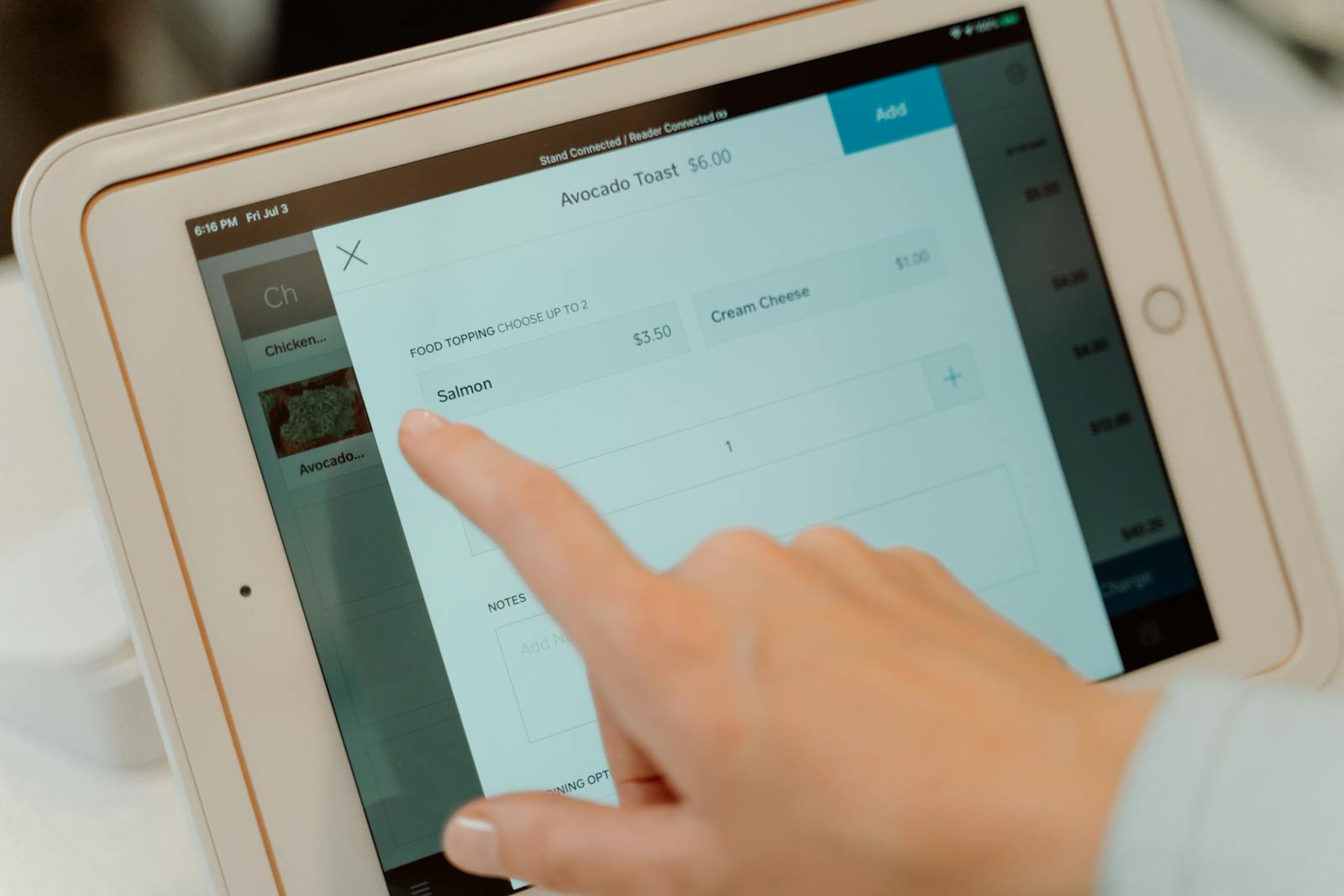 Close-up of a person's finger interacting with a point of sale tablet screen.