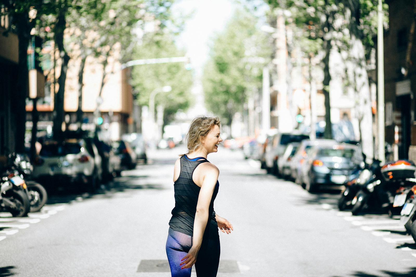 A woman in activewear, smiling while walking in a vibrant urban street.