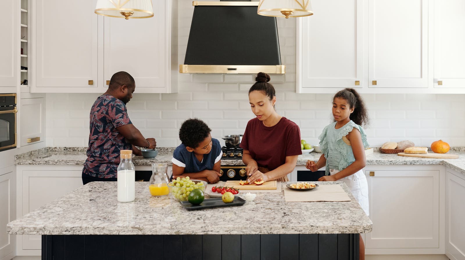Family of four cooking together in a bright kitchen, chopping fruits and enjoying time together.