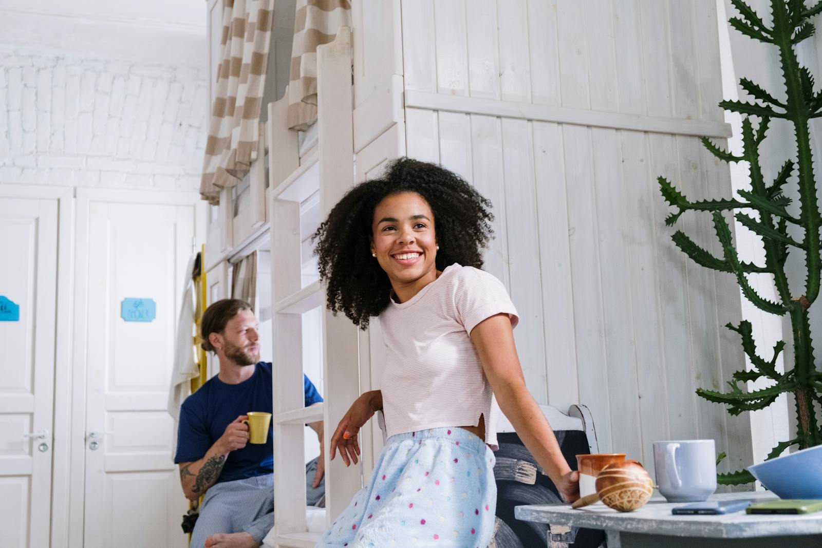 Joyful couple enjoying coffee together in a bright, cozy dorm room with a modern touch.