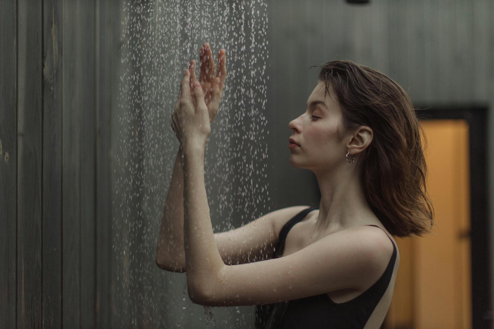 A woman savoring a tranquil moment under a gentle outdoor shower, side view.