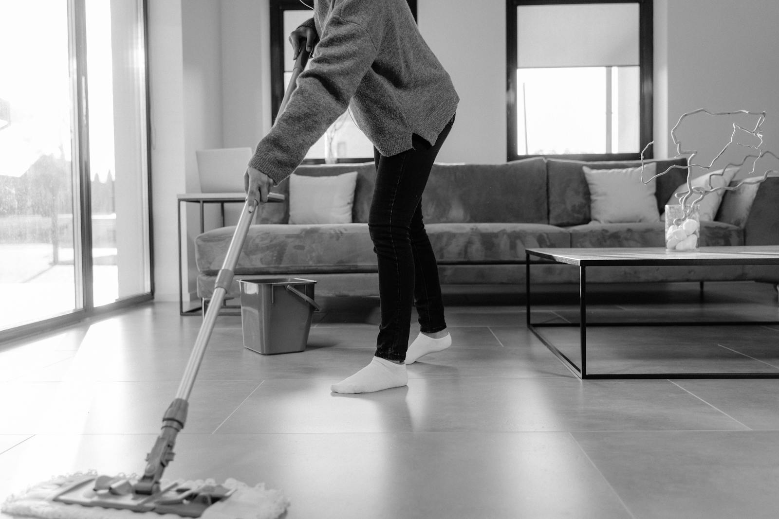 A grayscale photo of a person mopping the floor in a modern living room.