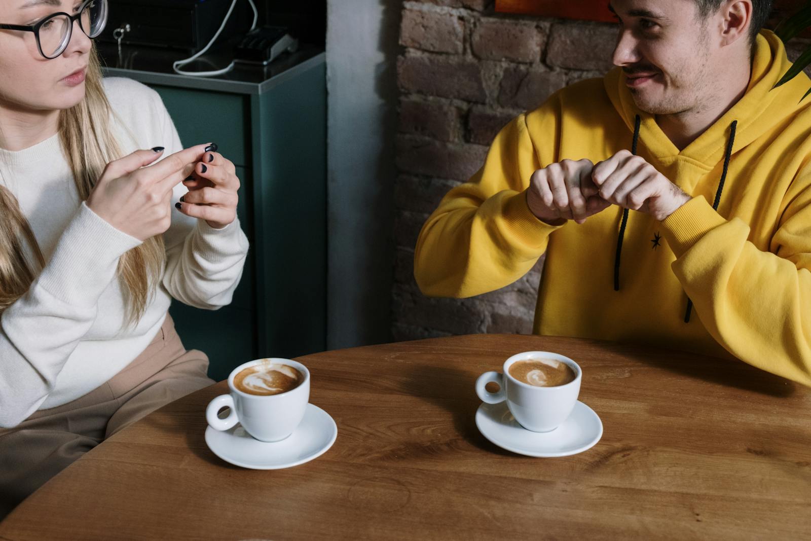 Two individuals communicating using sign language at a cafe table with coffee cups.