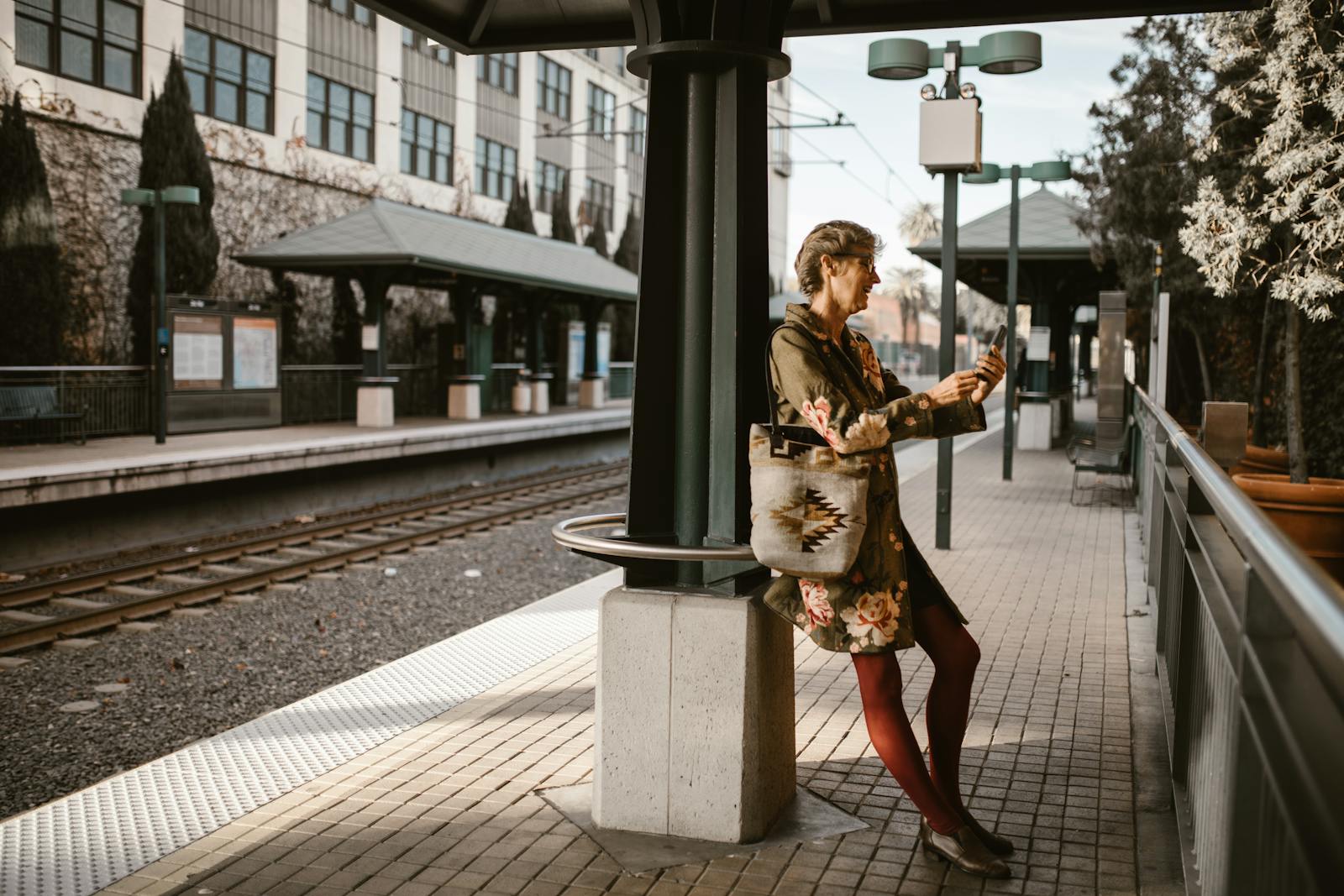Stylish woman using smartphone at urban train station on a sunny day.