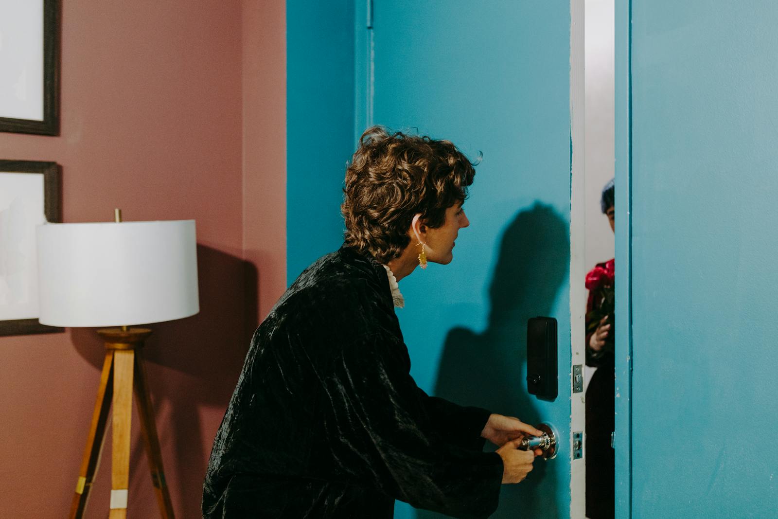 A person at a blue door surprised by a visitor holding flowers indoors.