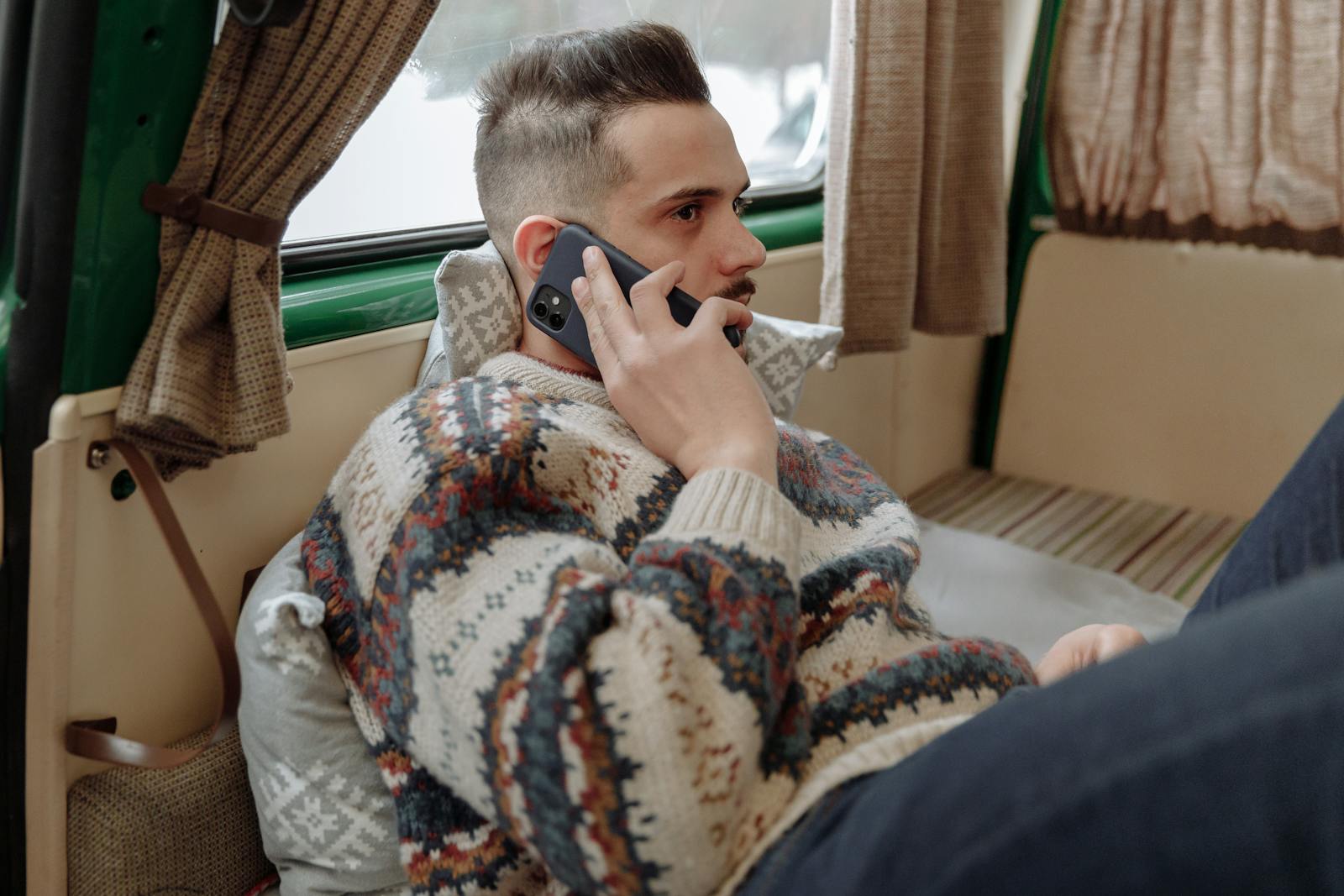 Casual adult man wearing sweater, relaxing indoors while talking on phone.