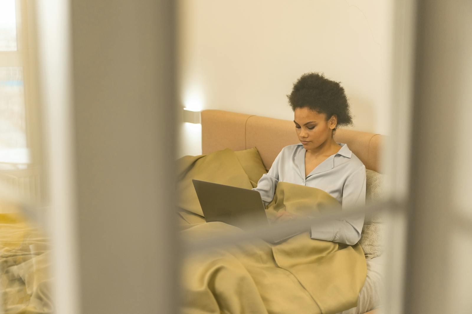 Young woman working on a laptop in bed, showcasing modern remote work lifestyle.