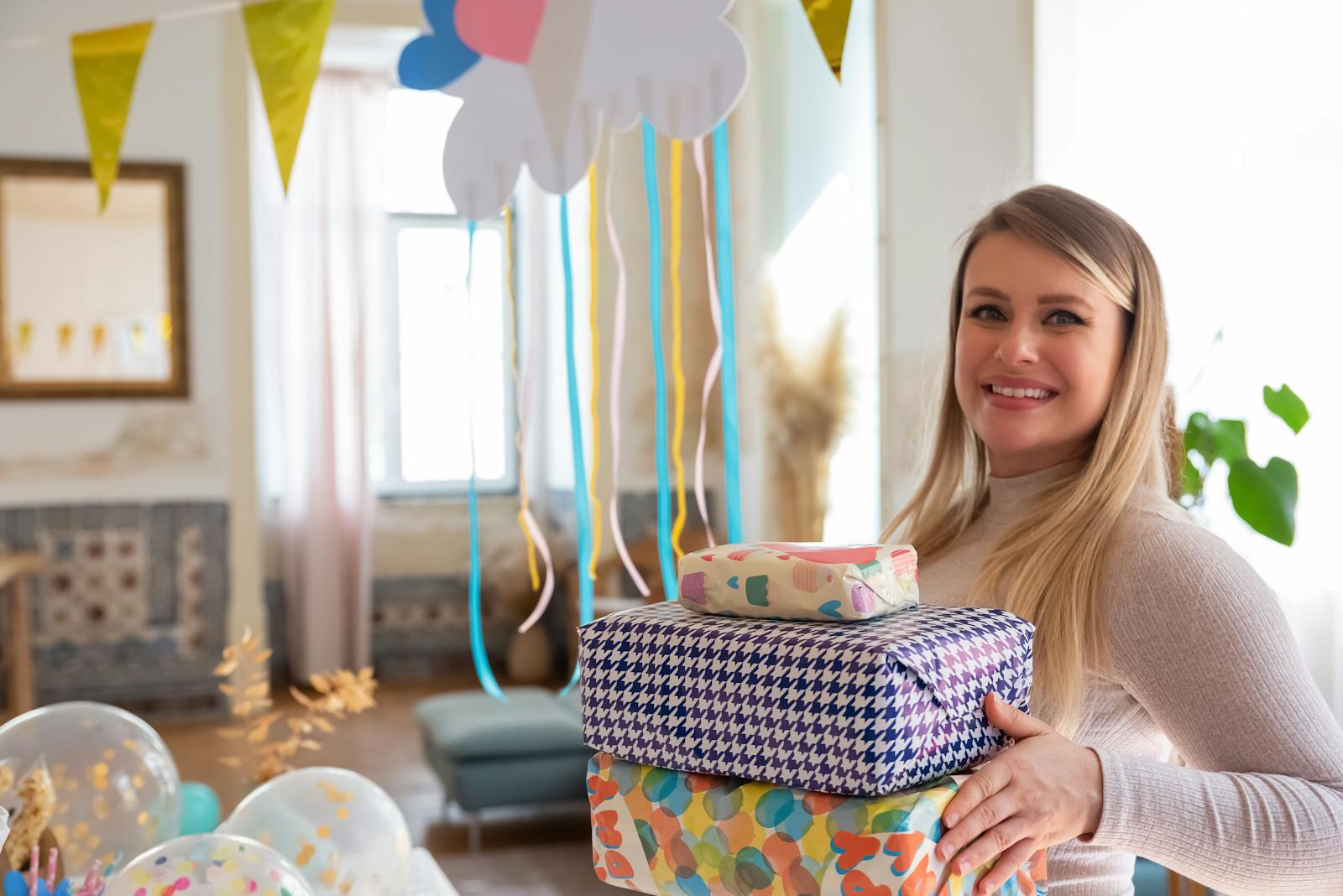 Happy woman holding colorful gift boxes at a festive baby shower party indoors.