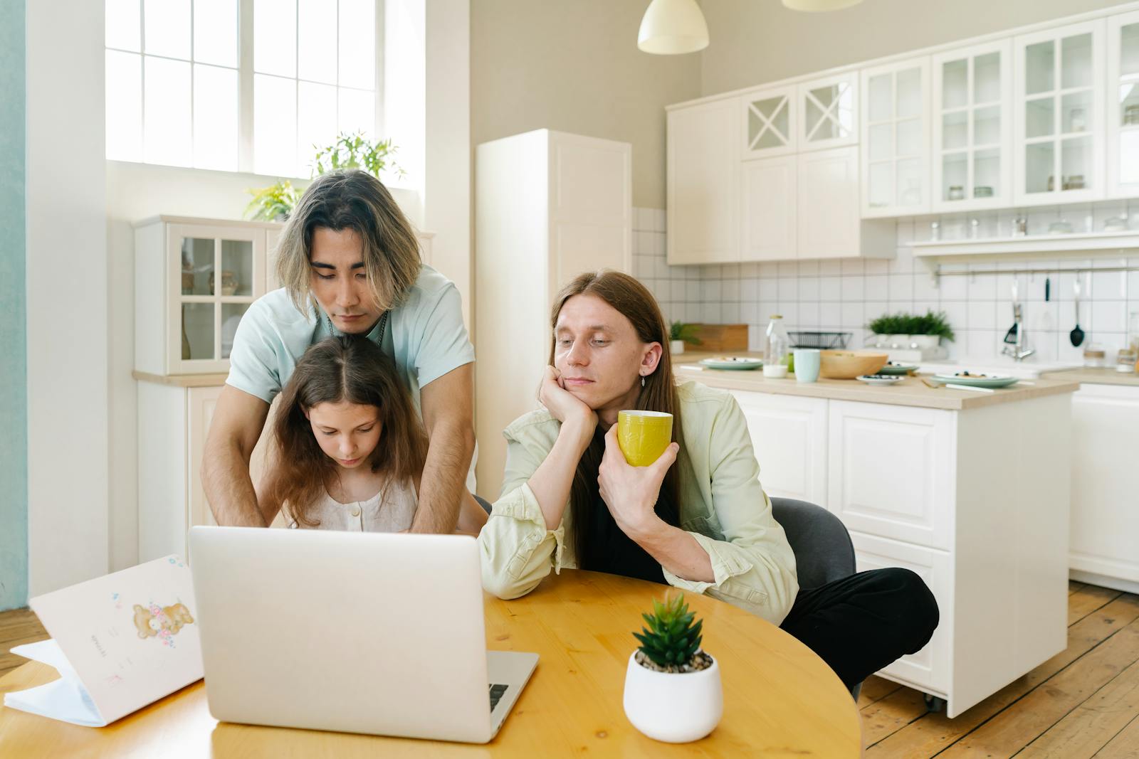 A family spends quality time together in a modern kitchen, focused on a laptop.