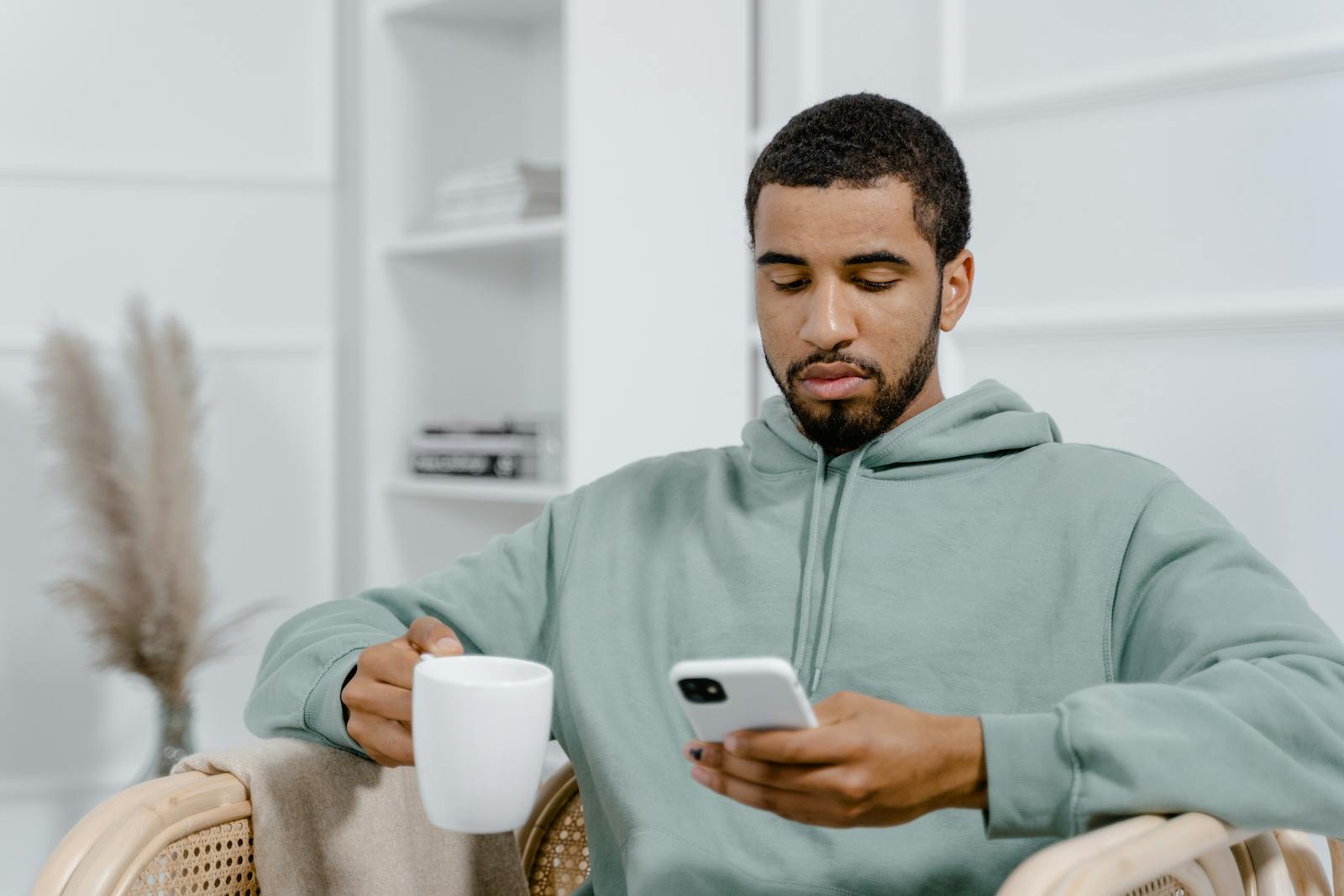 Man in a cozy setting using smartphone and holding a coffee mug.