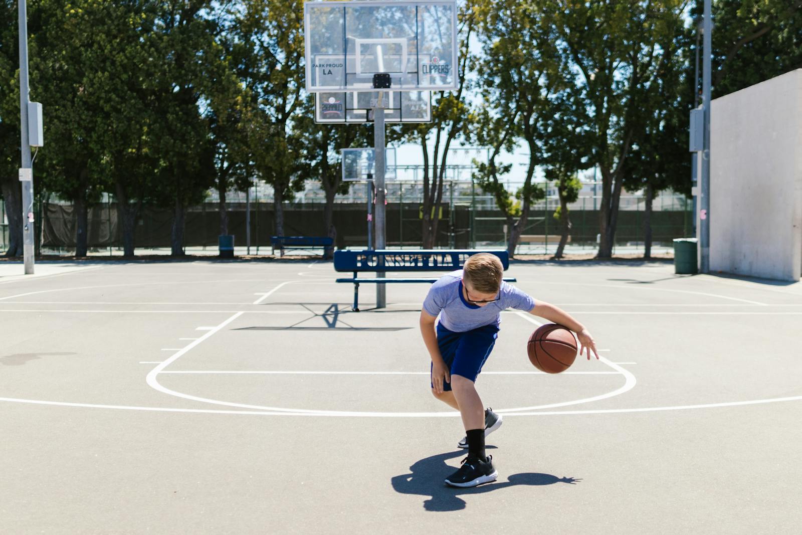 A young boy dribbles a basketball on an outdoor court on a sunny day, showcasing sports and play.