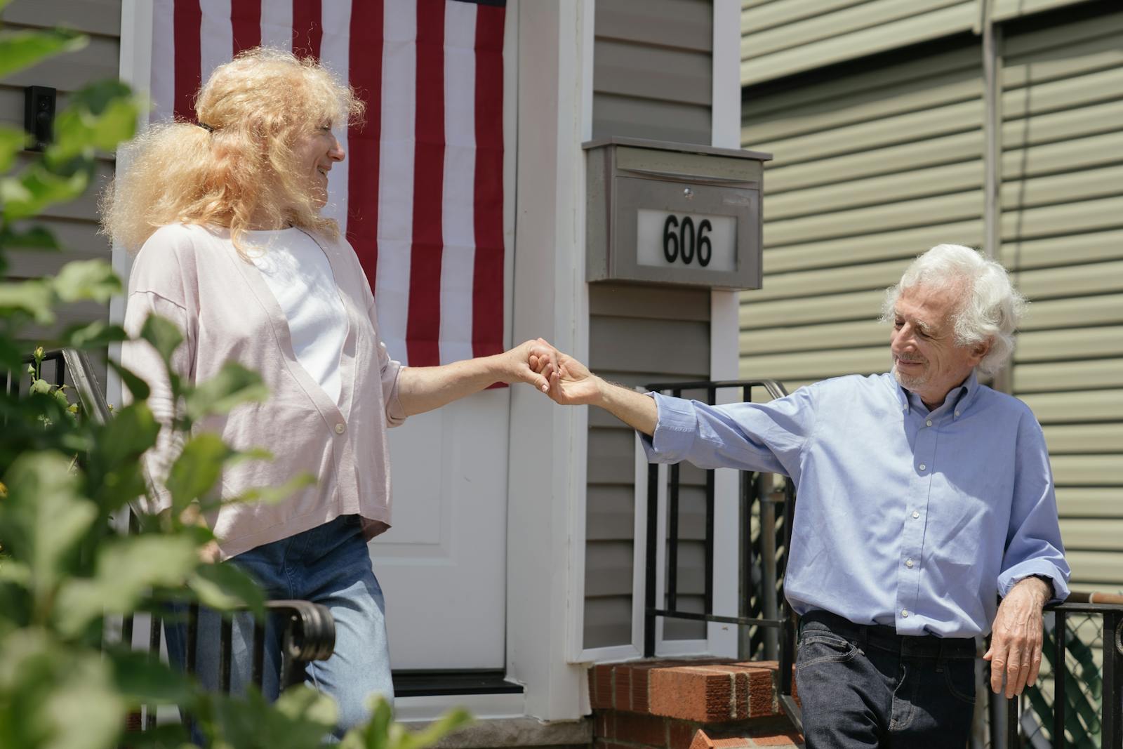A happy elderly couple holding hands outside their home on a sunny day.