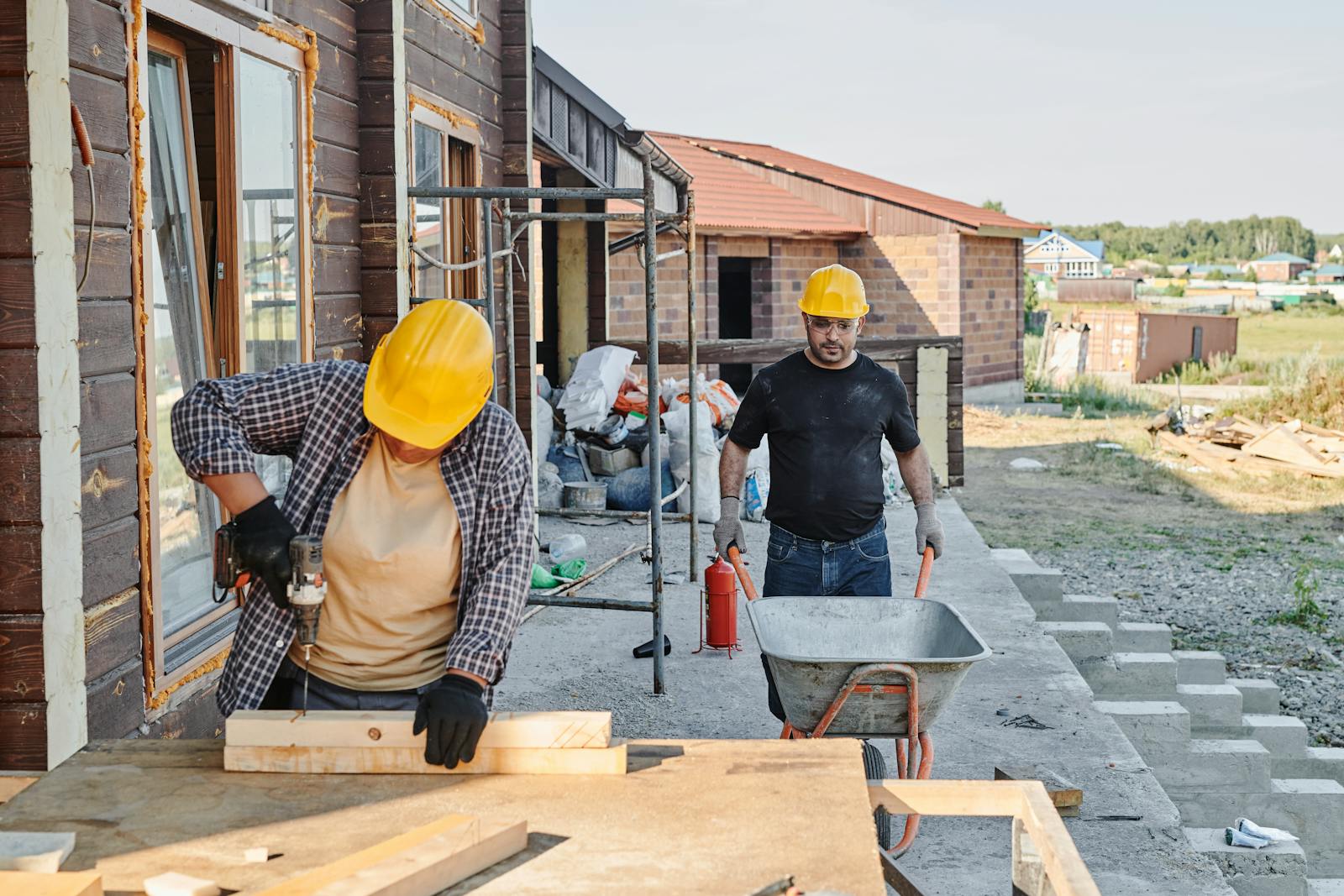 Construction workers building a house, using a saw and carrying materials in a wheelbarrow.