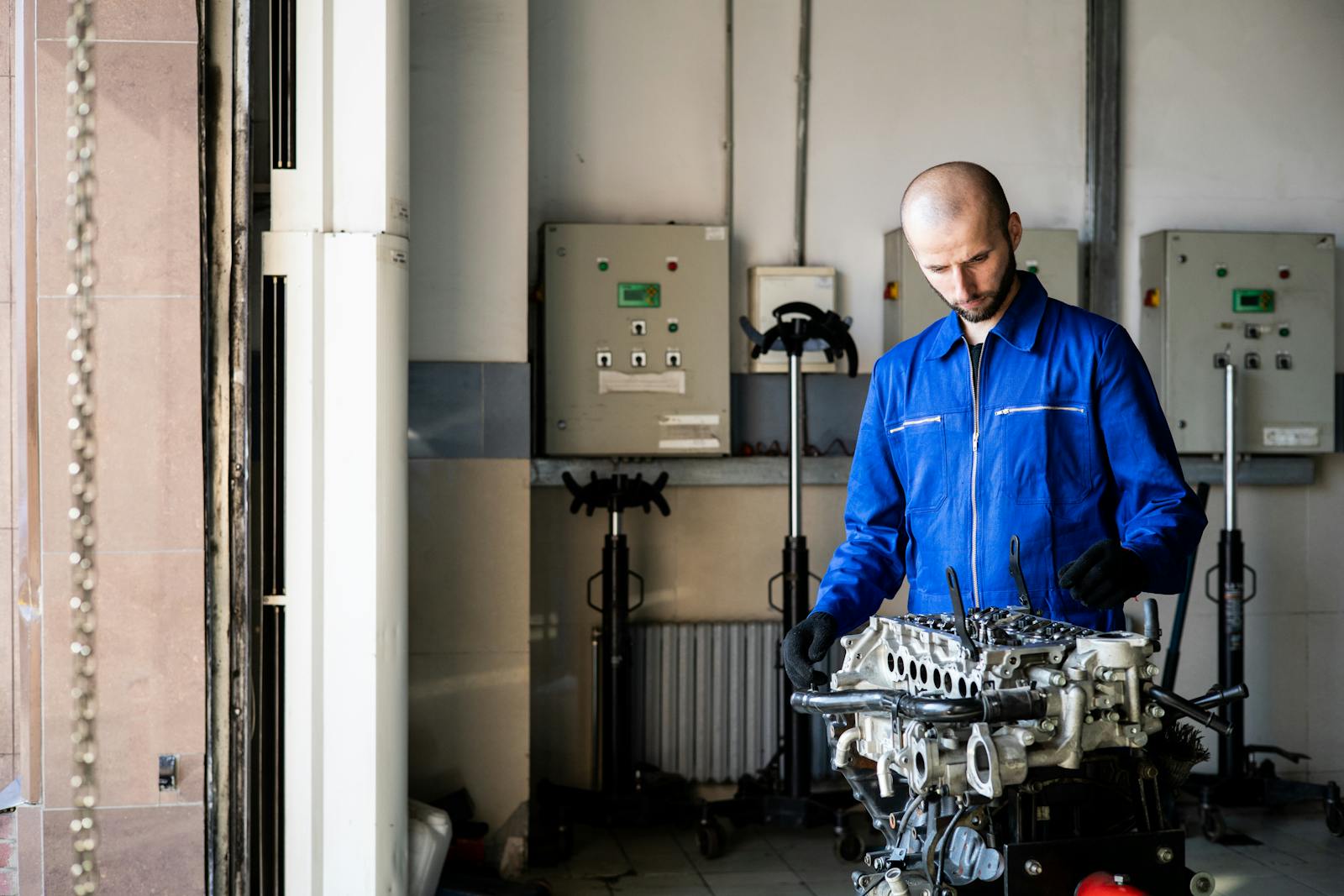 A mechanic in blue coveralls inspects an engine in a repair shop.
