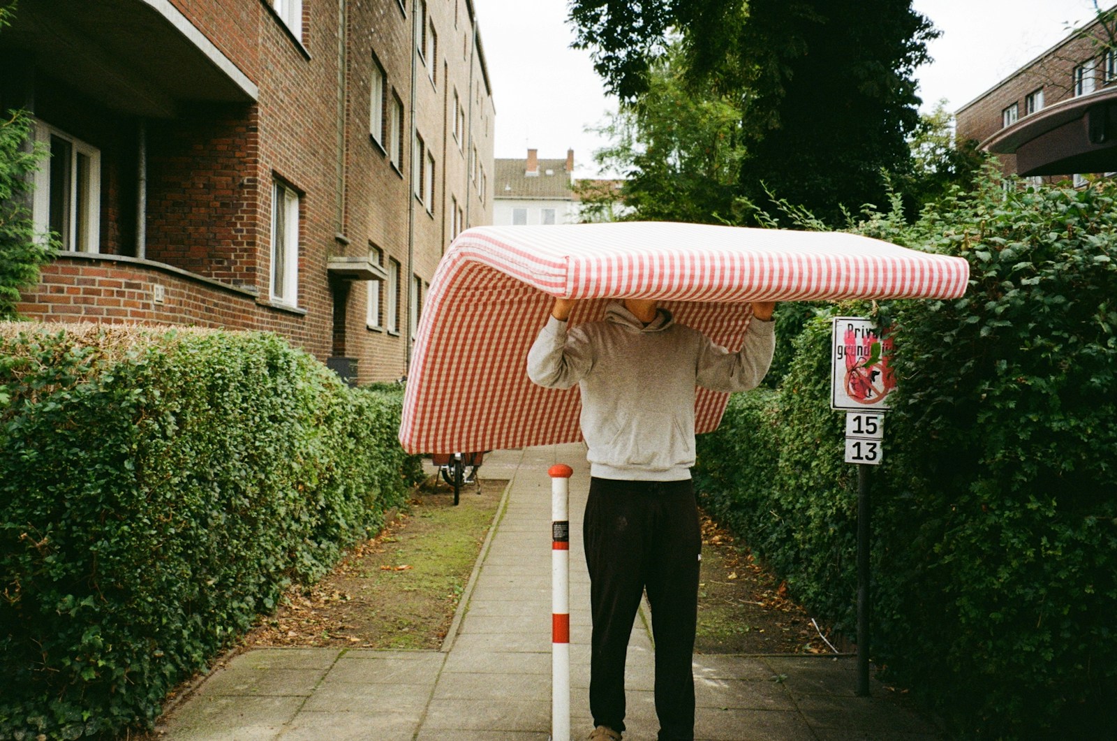Man carrying a mattress down a sidewalk.