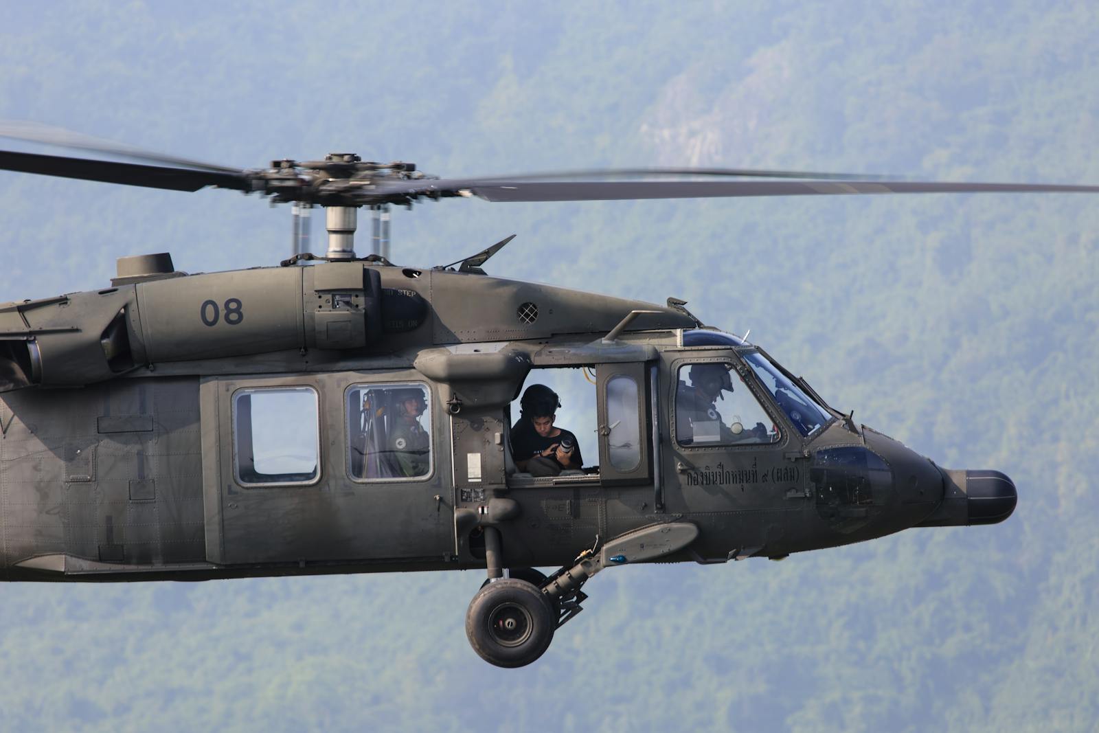 A military helicopter flying with crew visible, showcasing aerial operations.