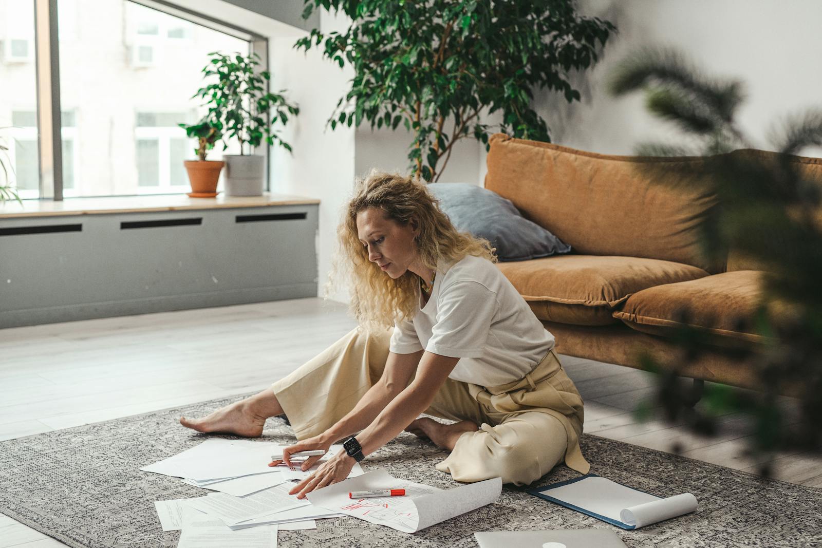 A woman sitting on the floor of her living room working on documents and papers, embodying a comfortable work-from-home atmosphere.