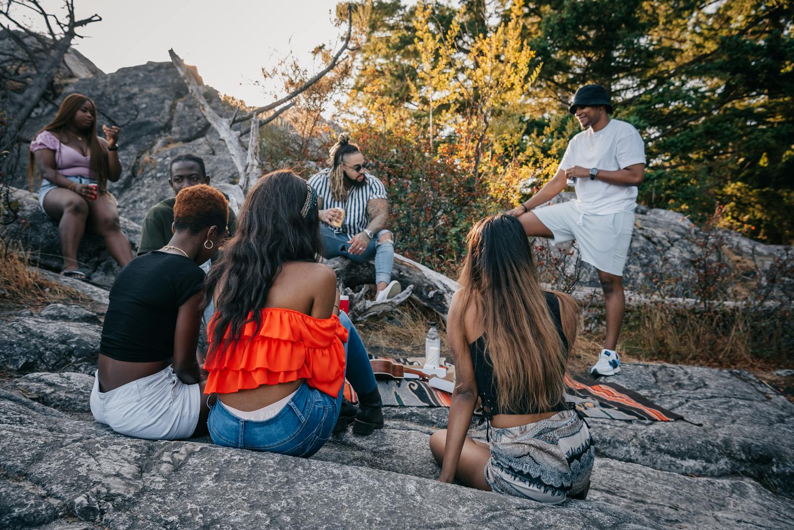 A group of friends enjoying a casual outdoor gathering on rocks surrounded by trees and nature.