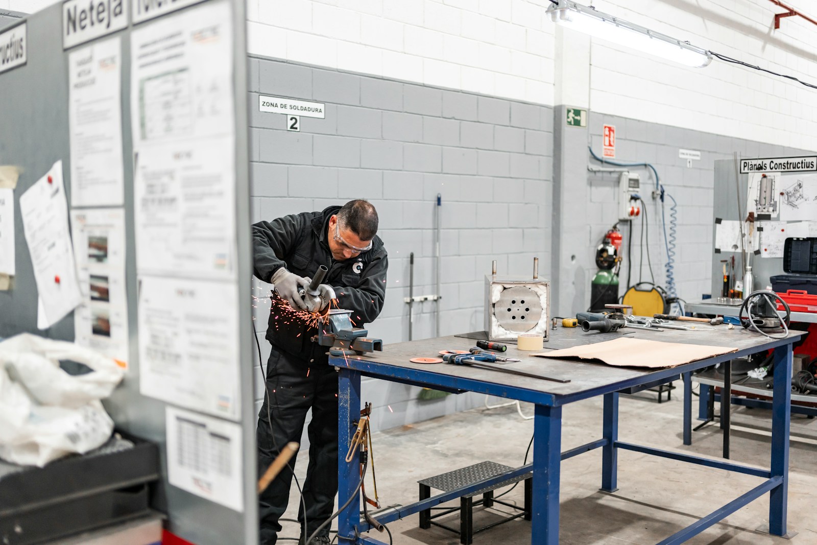 A worker is grinding metal in a workshop.