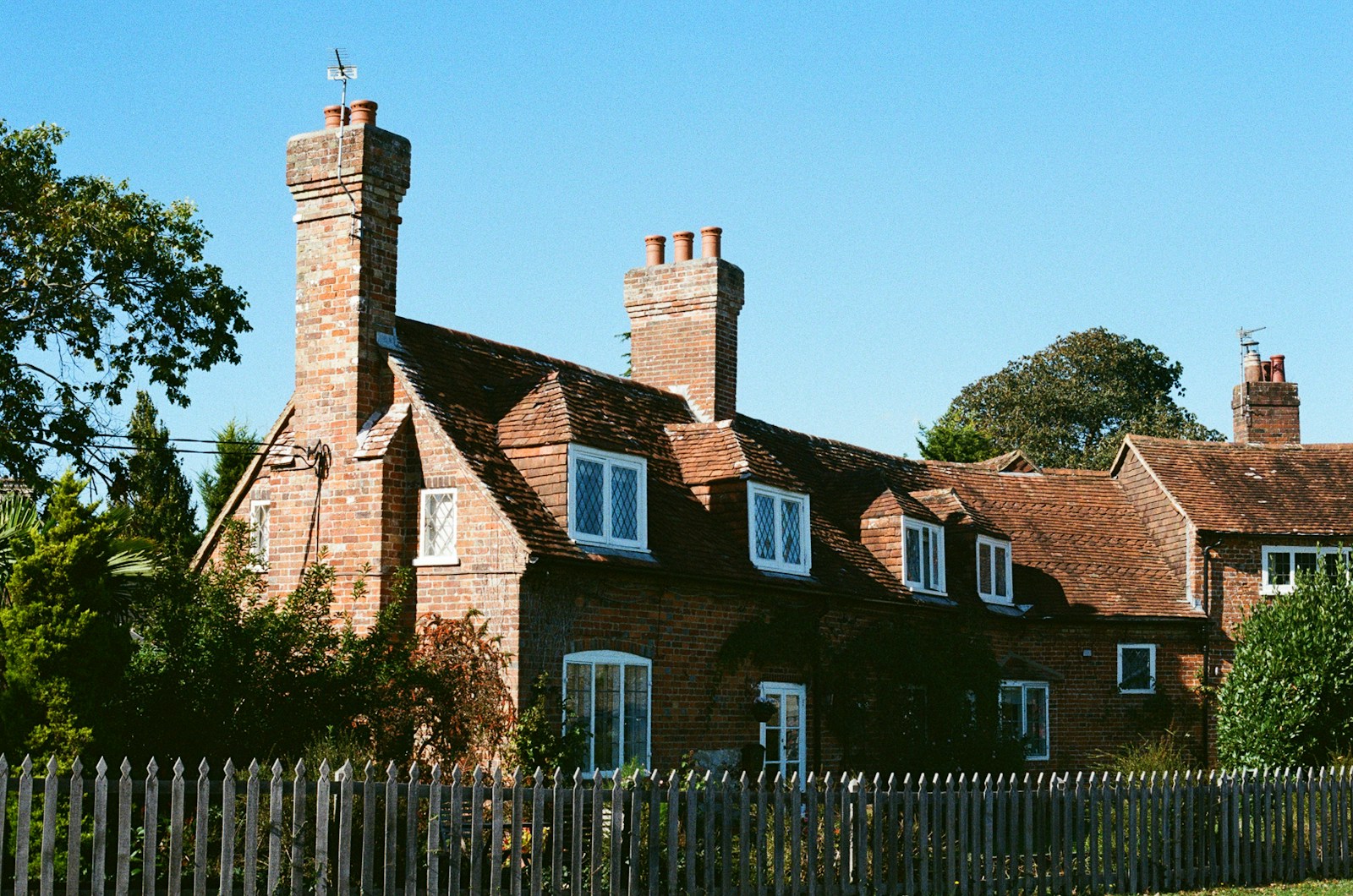 Brick cottage with multiple chimneys under blue sky.