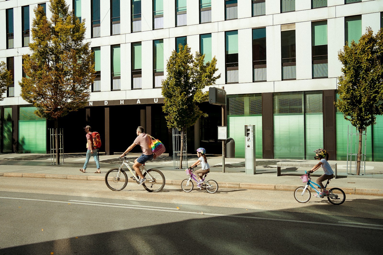 People cycling past a modern building on a sunny day.