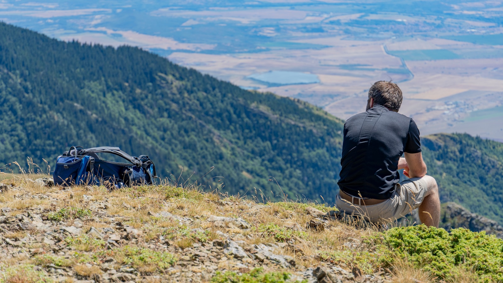 a man sitting on top of a hill next to a backpack