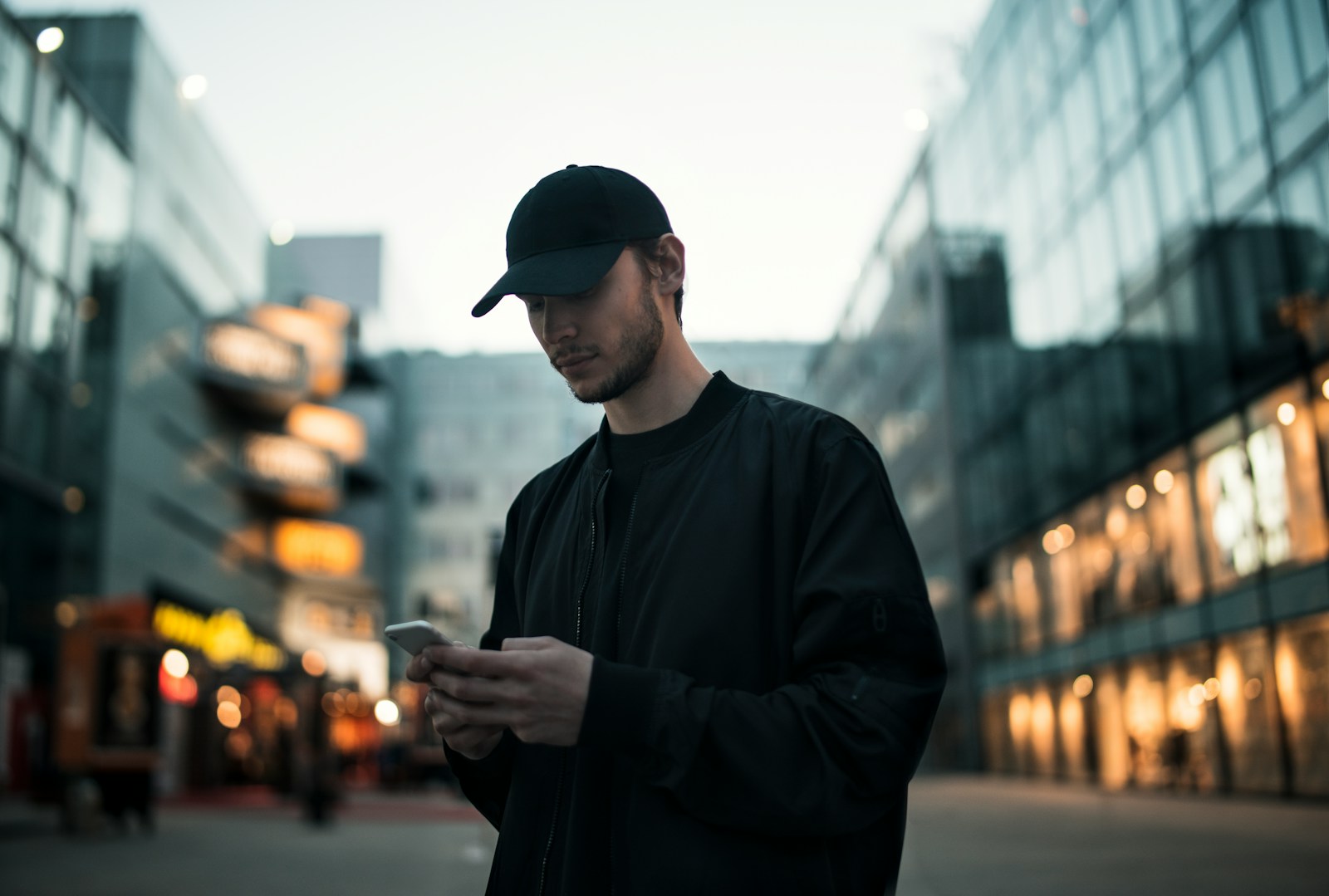 man in black jacket wearing black fitted cap while using phone