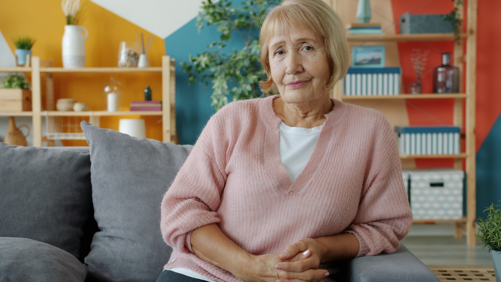 Elderly woman sitting on a couch in a colorful room.