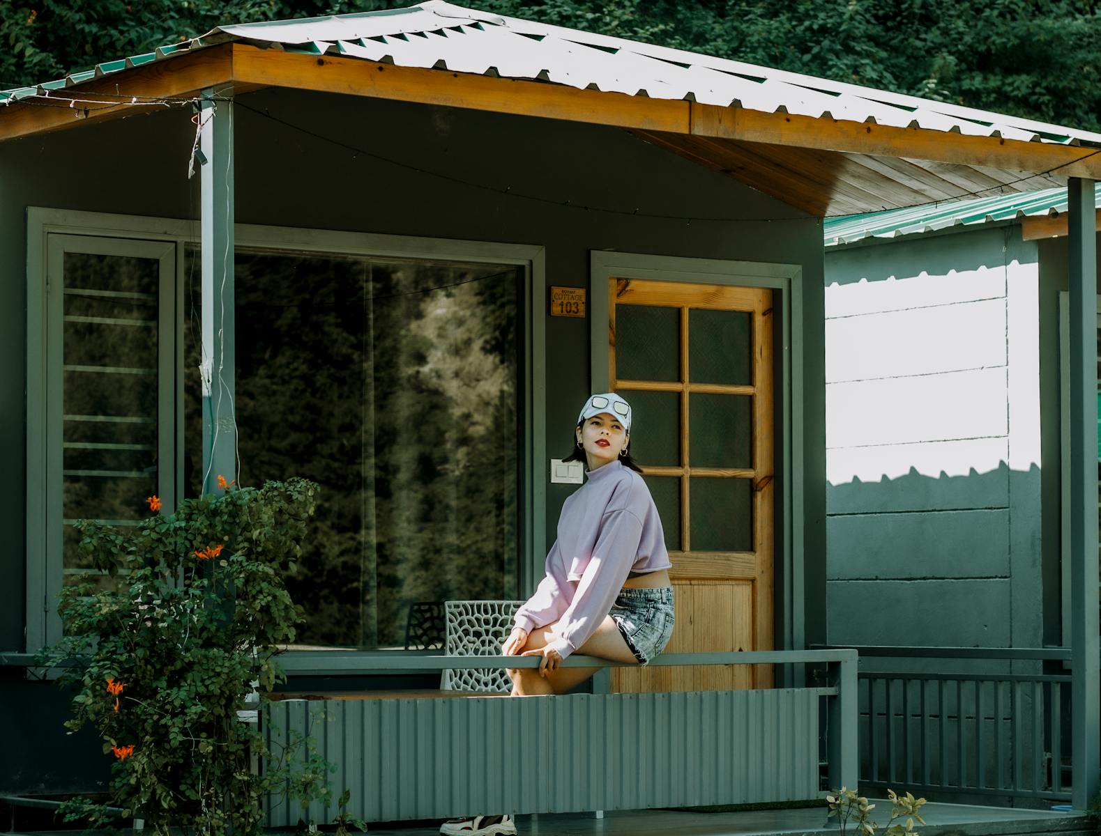 A stylish woman sitting on a porch railing, enjoying a sunny day outdoors.