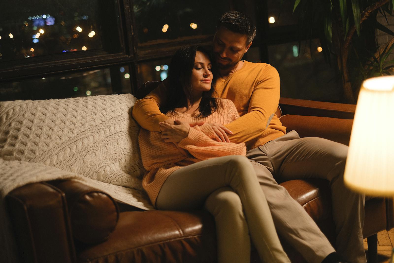 A couple embraces on a couch in a softly lit room, creating a warm and cozy atmosphere.