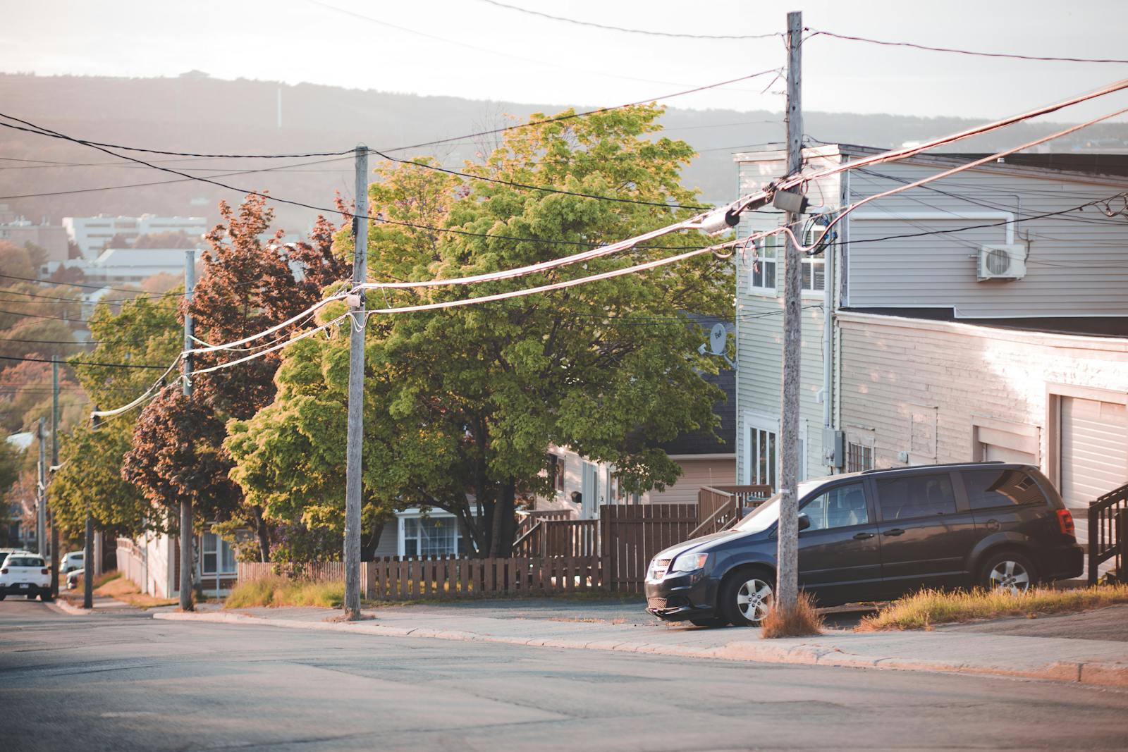 A black SUV parked on a suburban street lined with trees and houses on a sunny day.