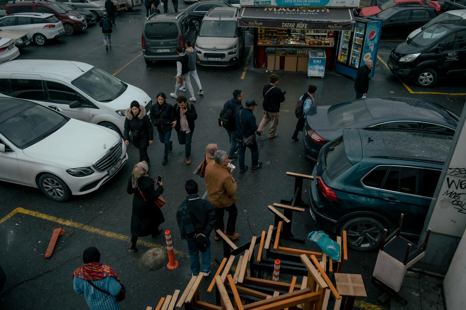 A bustling urban parking lot with people walking and various parked cars, capturing daily life activity.
