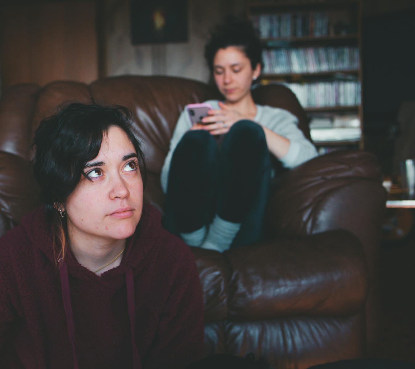 A cozy indoor scene with two women, one using a phone and the other gazing thoughtfully.