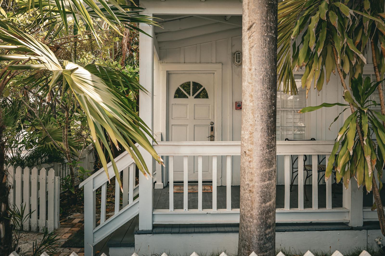 Charming tropical front porch with palm trees and white wooden railing, evoking a summer vibe.