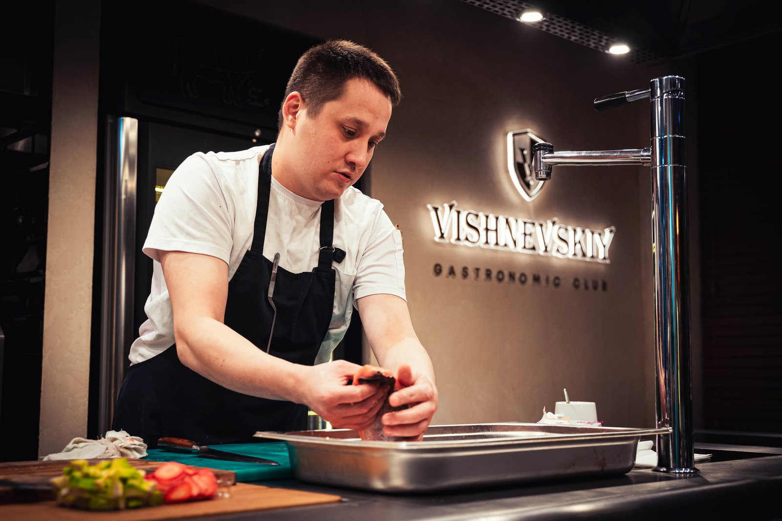 Chef wearing an apron prepares gourmet food in a professional kitchen.