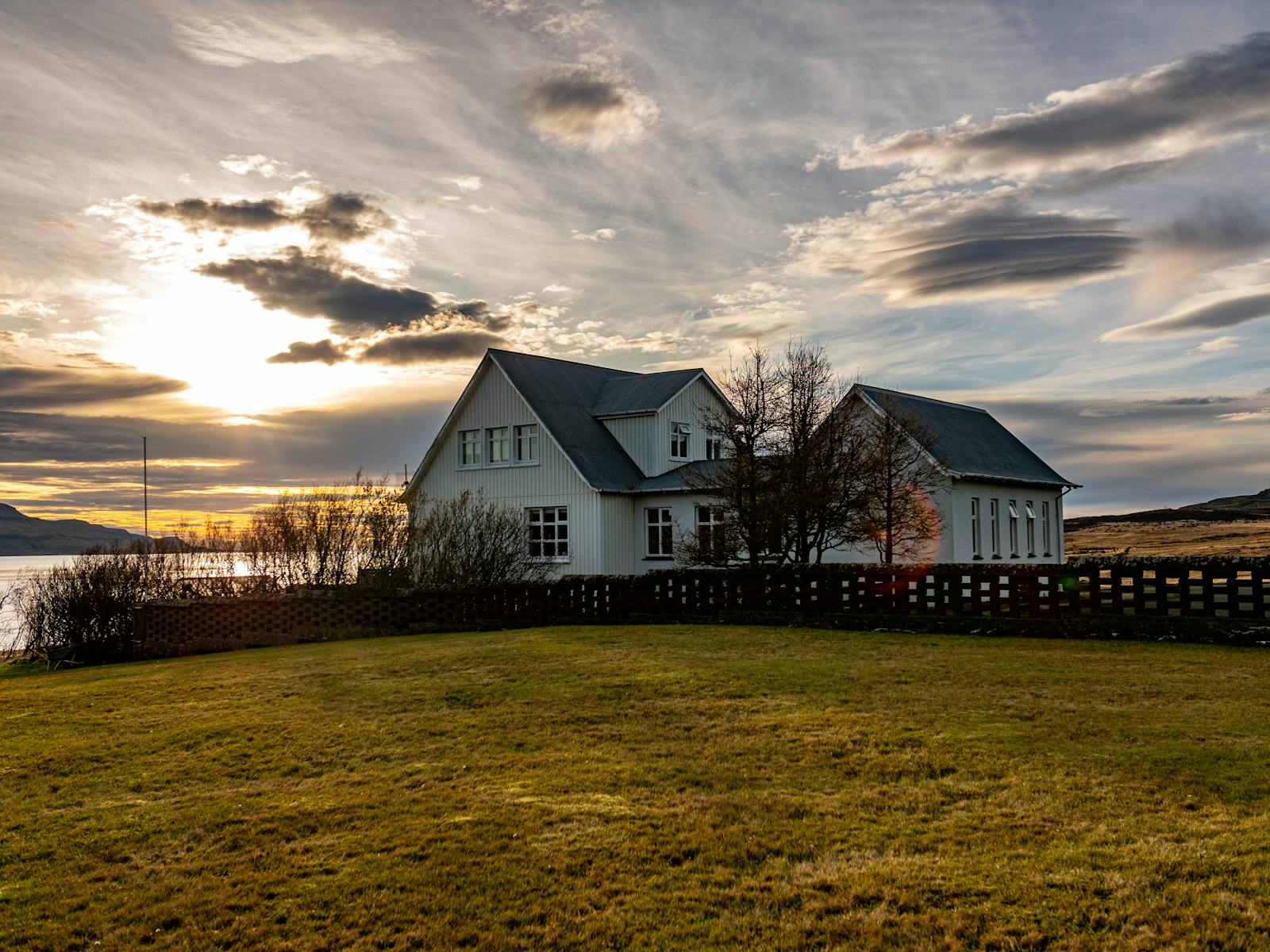 Idyllic countryside house near a calm lake during sunset, with stunning cloud patterns.