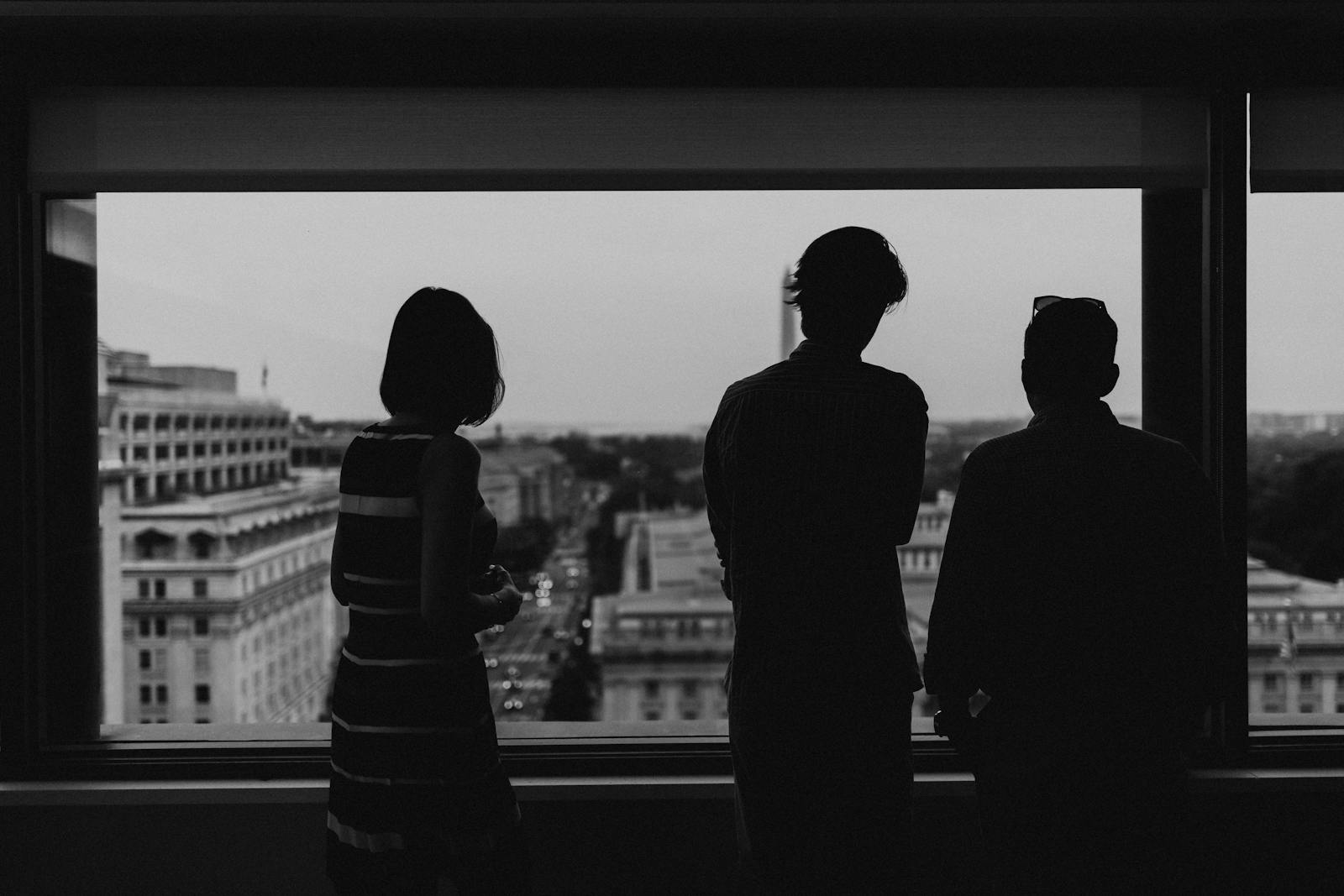 Silhouette of three people viewing Washington DC from a high-rise window at dusk.