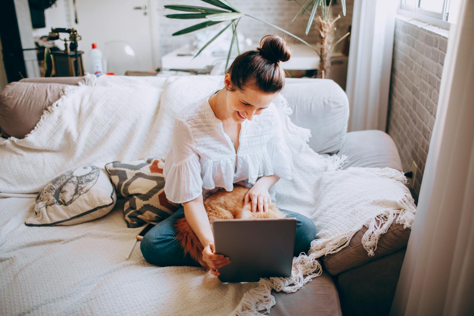 Woman sitting on sofa with tablet, relaxed and at home, enjoying leisure time with a pet cat.