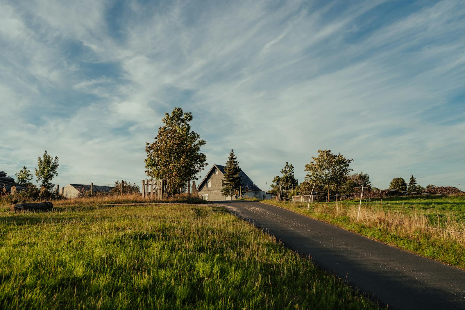 Charming countryside scenery featuring a paved road leading to a farmhouse surrounded by lush fields.