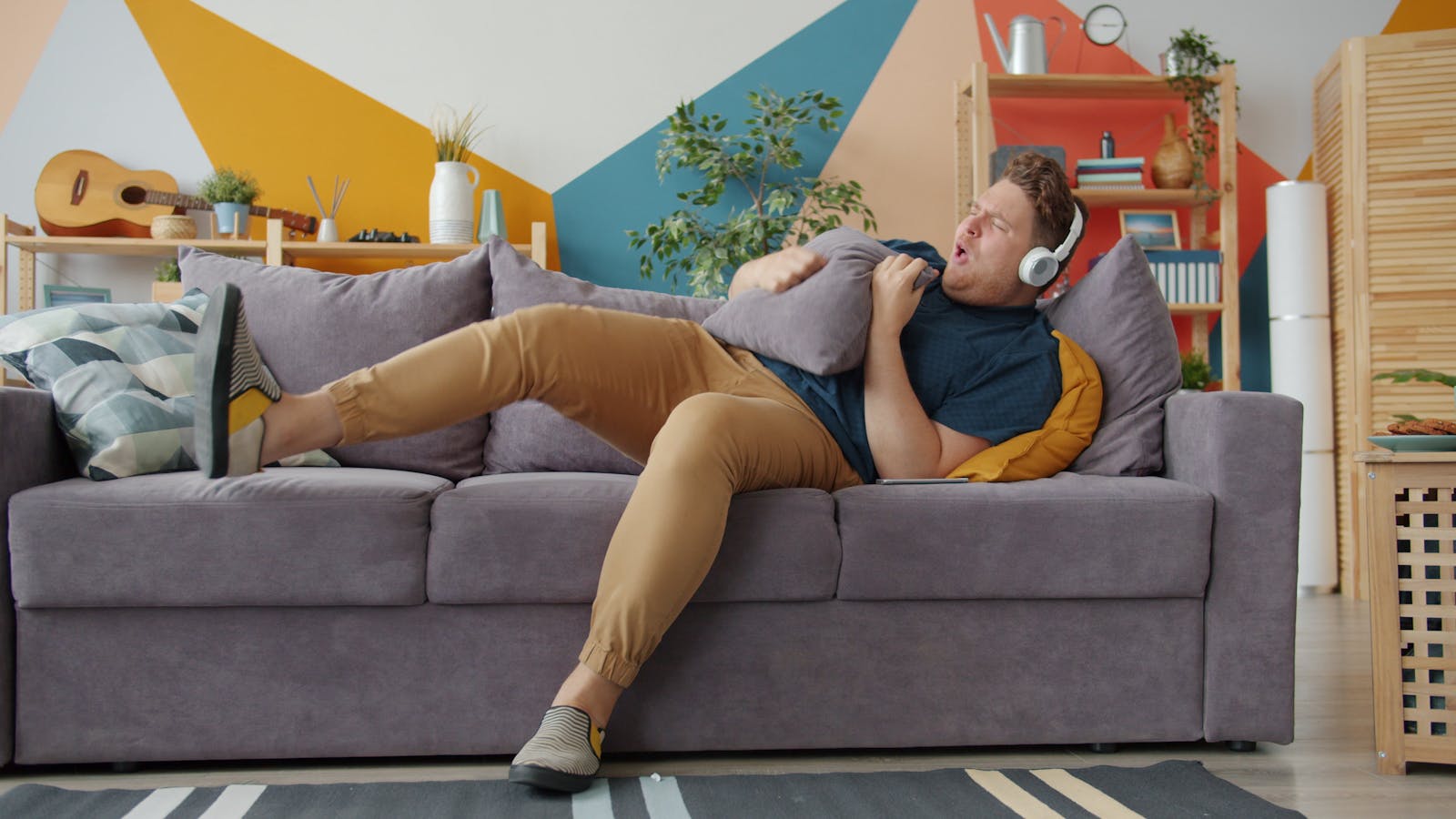 A young man enjoying music with headphones on a colorful couch indoors.