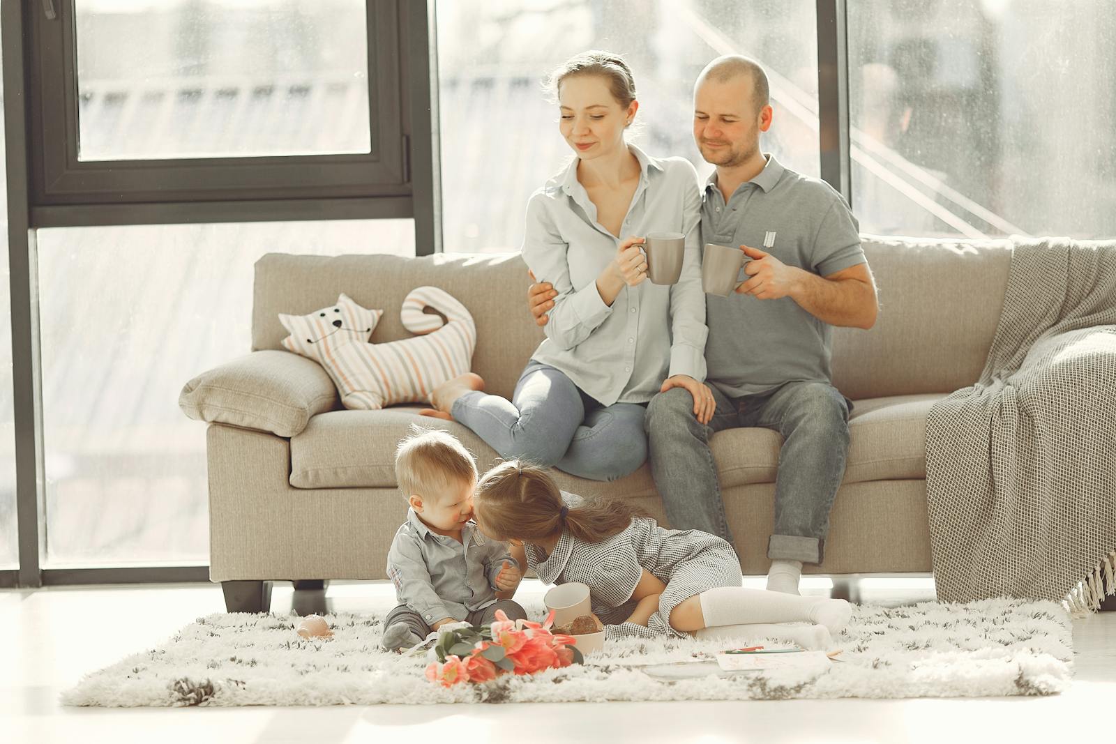 Cheerful family smiling while spending weekend together sitting parents sitting on comfortable sofa while children resting on carpet and playing