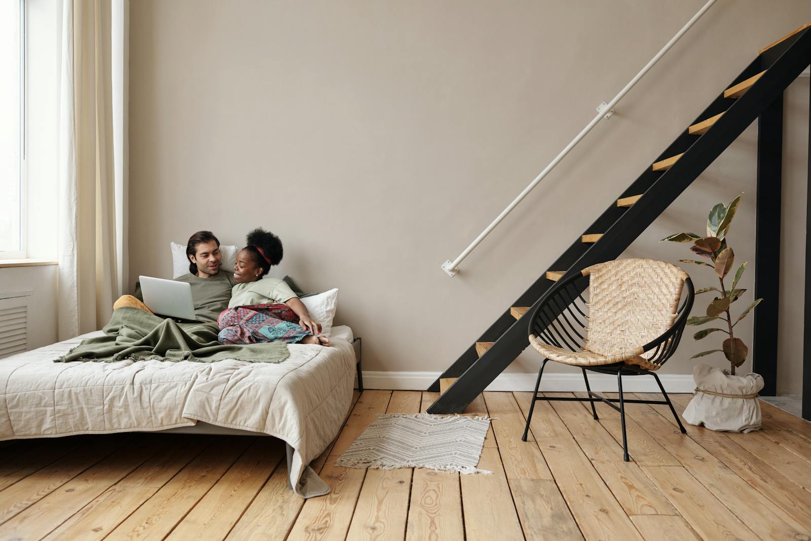 A couple enjoys a relaxing day indoors, embracing on a bed with a laptop in a stylish apartment.