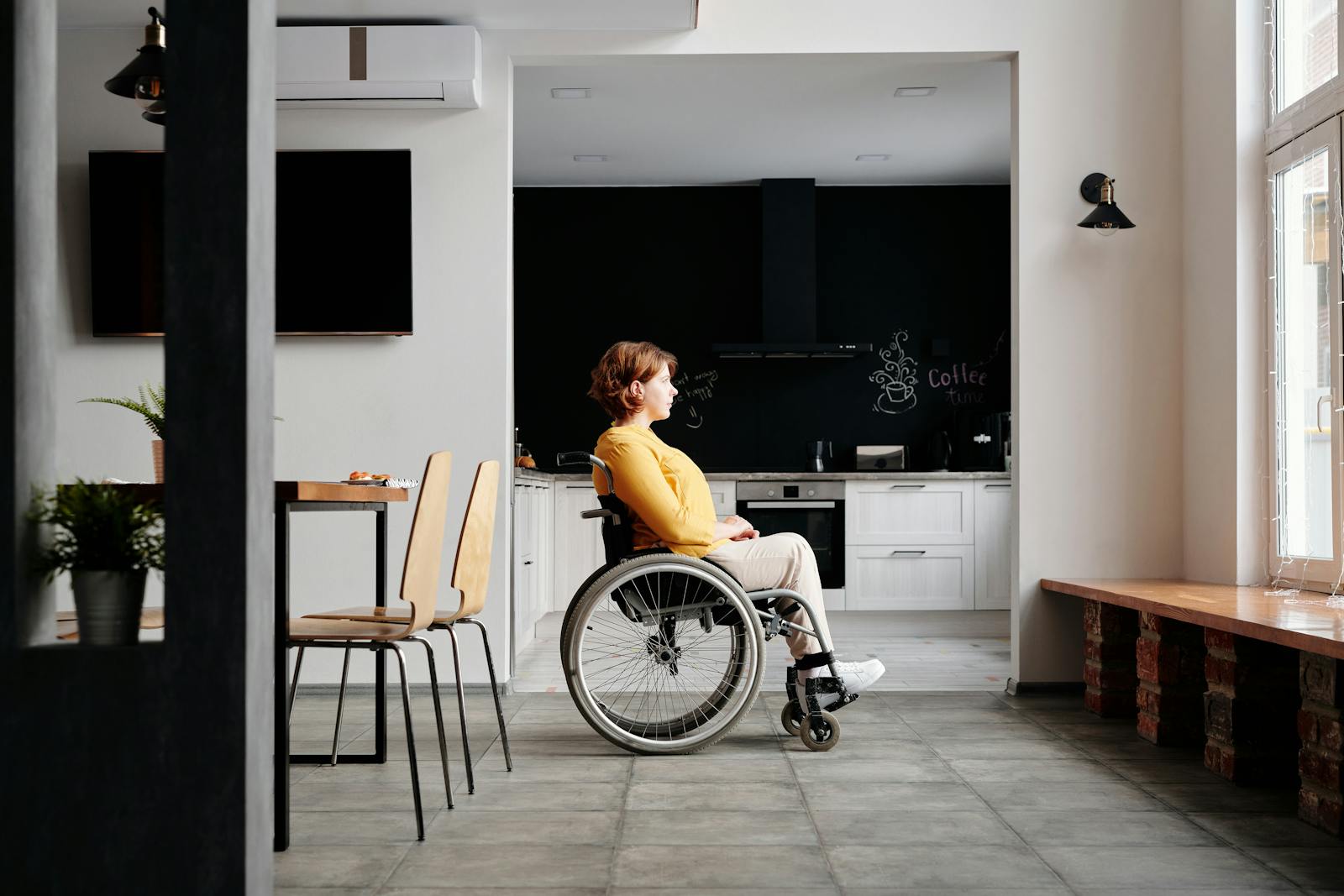 Woman in a wheelchair gazing outside from a modern home with stylish decor.