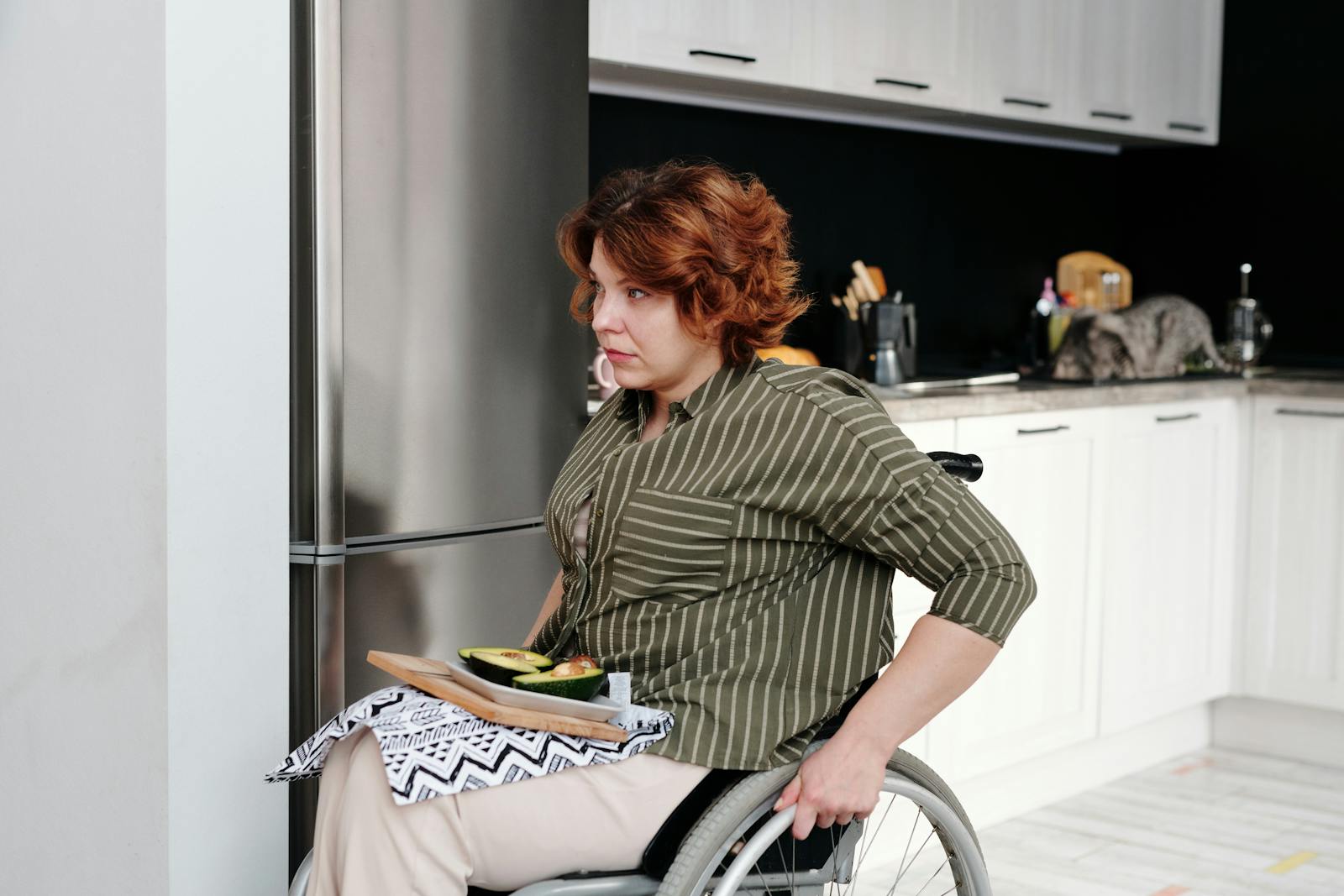 Woman seated in a wheelchair in a modern kitchen, preparing food on a cutting board.
