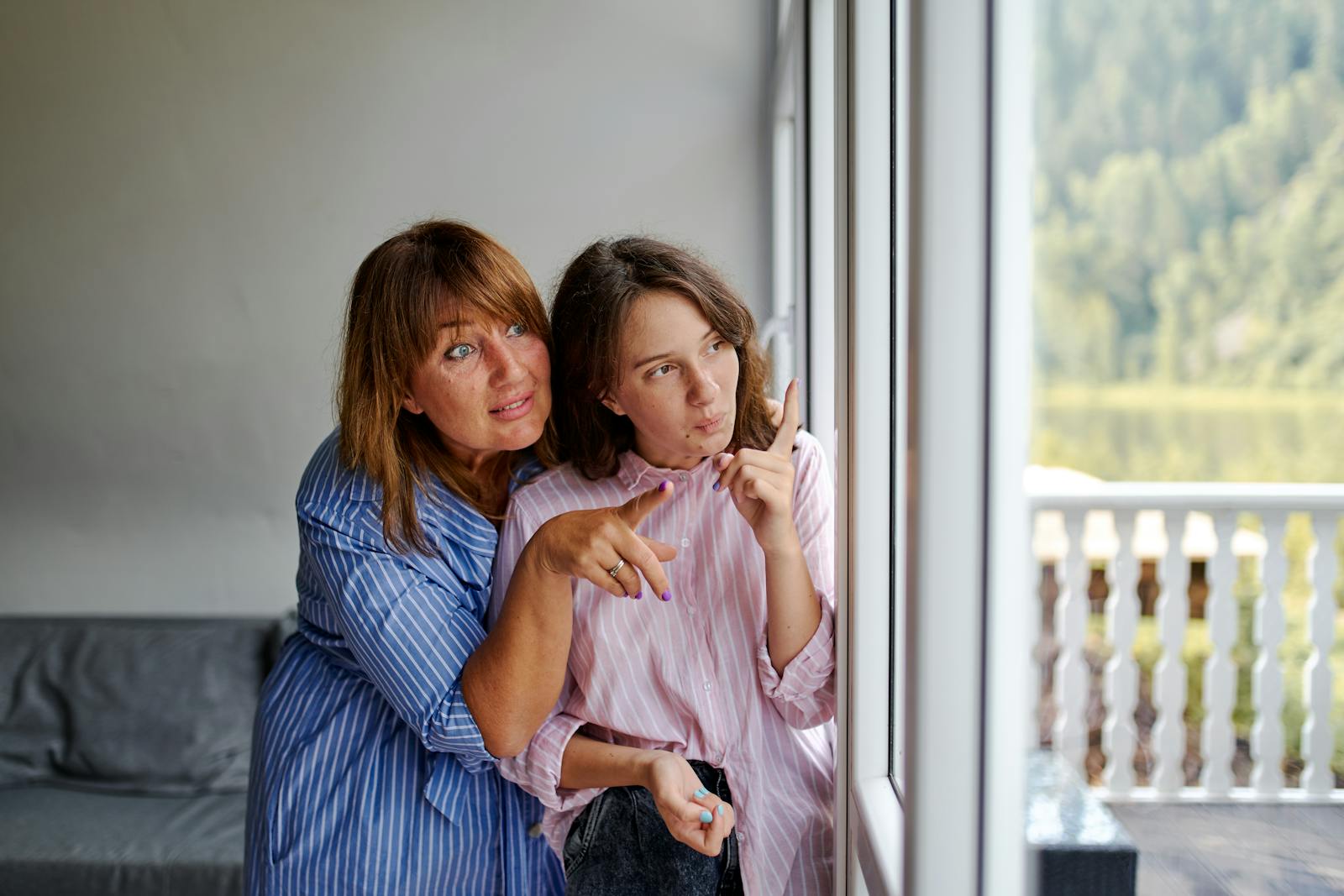 Females in stripped clothes snuggling each other pointing fingers at objects outside window