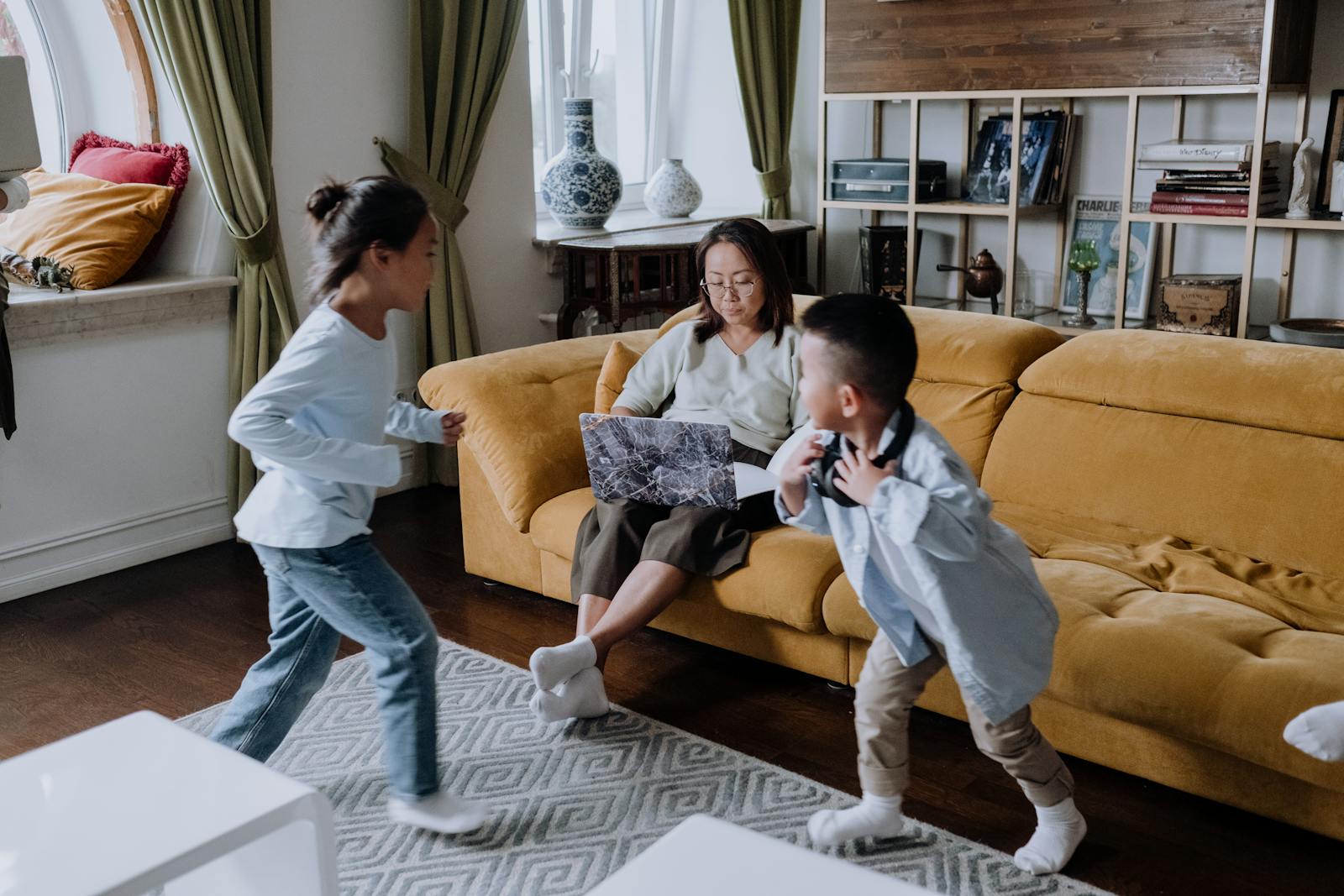 Mother with laptop watching her children play in a cozy living room setting