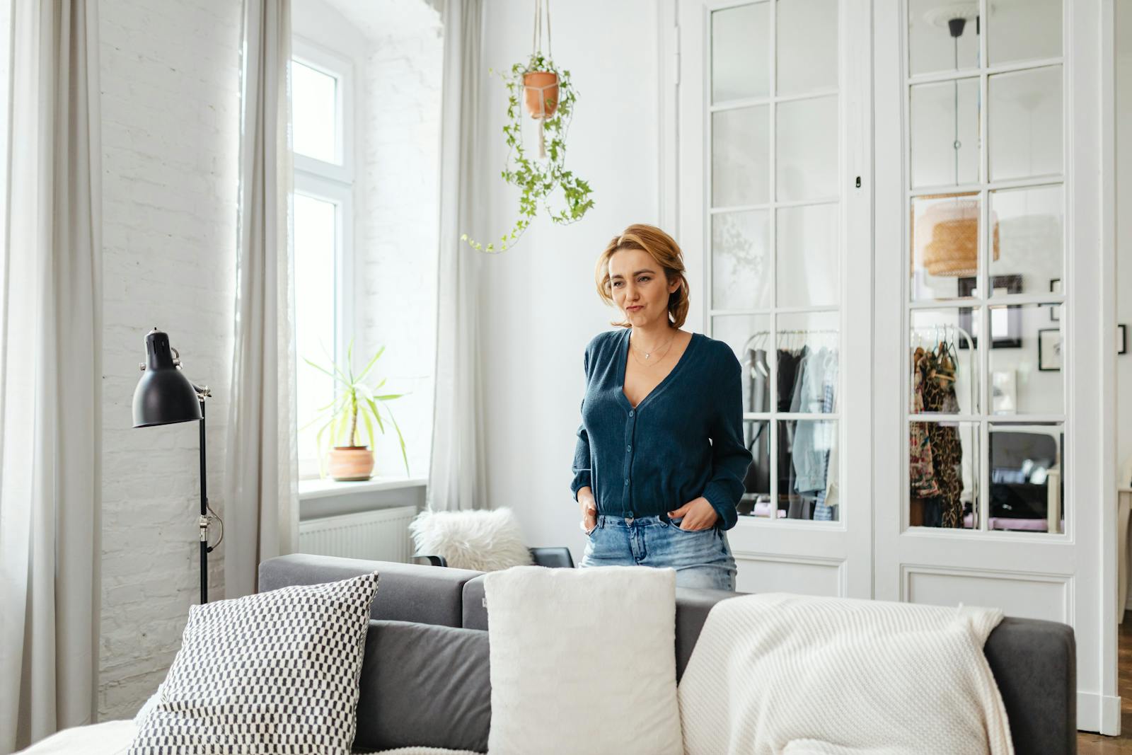 Woman in a relaxed pose standing in a stylish, well-lit living room with minimalistic decor.