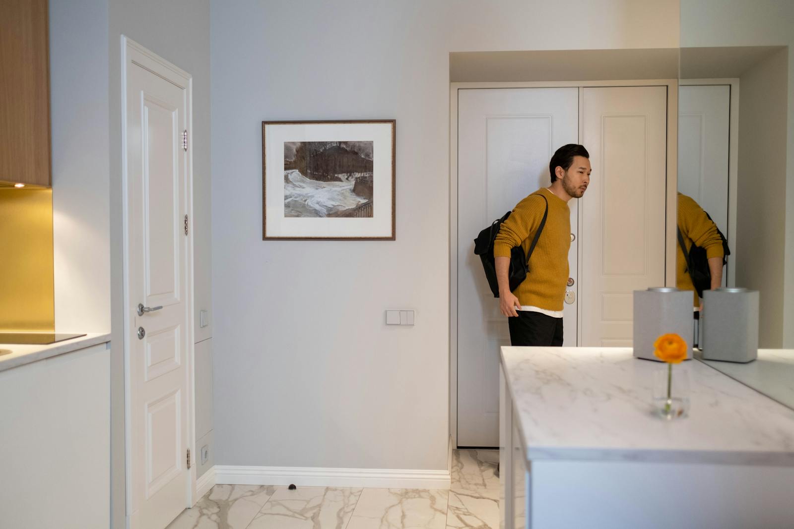 Asian man with bag entering a modern, well-lit interior room with minimal decor.