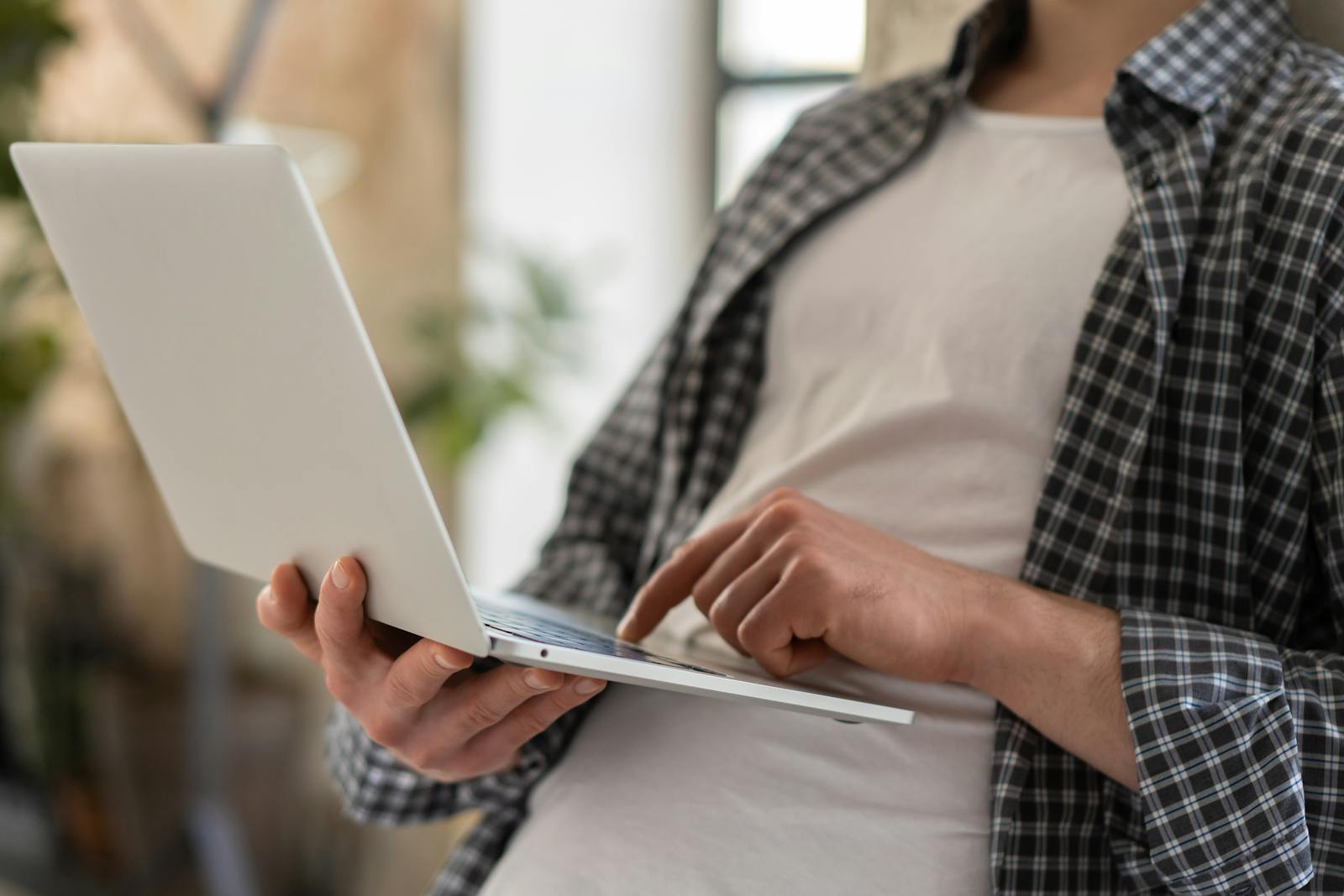 Young adult in casual shirt using a laptop indoors with blurred background and shallow focus.