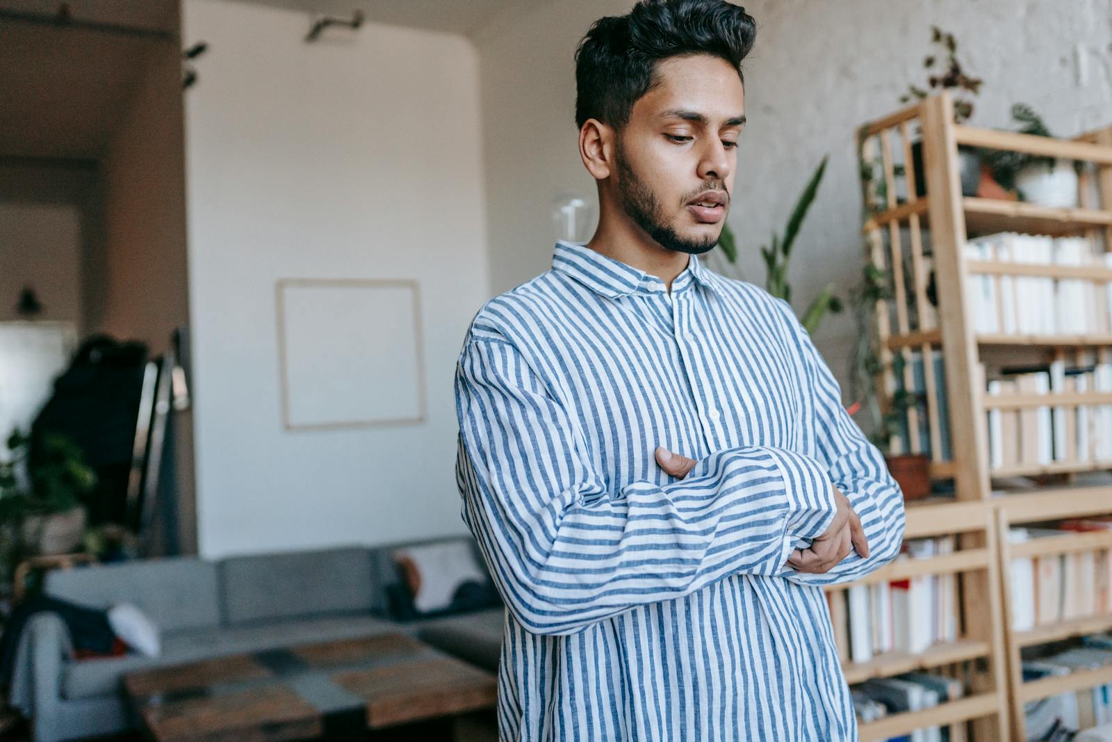 A young man in a striped shirt stands in prayer inside a modern home, embodying peace and reflection.